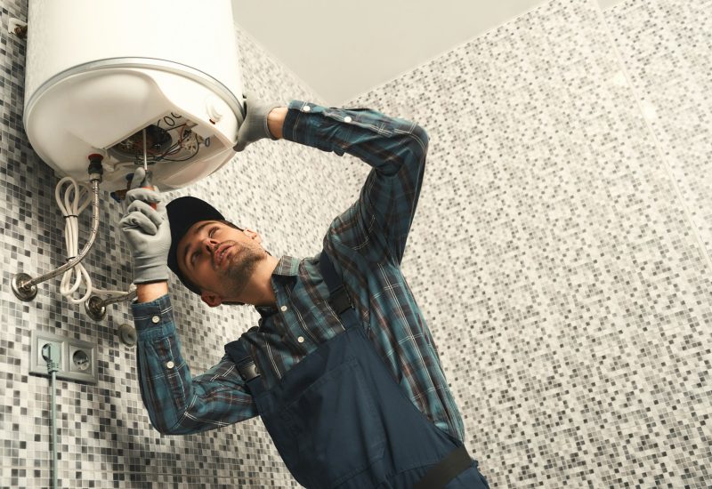 Plumber installing electric heating boiler. Young handyman in uniform setting up electric heating